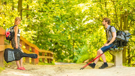 Adventure, tourism, enjoying summer time together - Hiking young couple with guitar backpack tramping on forest road sunny countrysideの写真素材