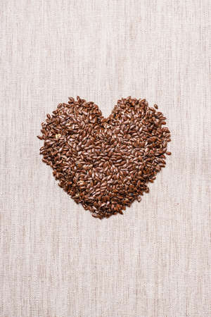Diet healthcare healthy food. Raw flax seeds linseed heart shaped on sack burlap background.の写真素材