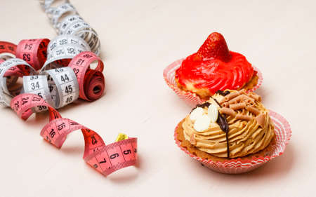 Appetite and gluttony concept. Fattening problem. Cakes cupcakes with measuring tape on tableの写真素材
