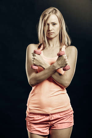 Fitness, sport, training and lifestyle concept. Fit woman with dumbbells flexing muscles in gym. Muscular blonde girl lifting light weights studio shot on black backgroundの写真素材