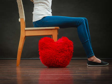 Broken heart love concept. woman sitting on chair red heart pillow on floor dark backgroundの写真素材