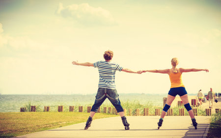 Holidays, active people and friendship concept. Young fit couple on roller skates riding outdoors on...