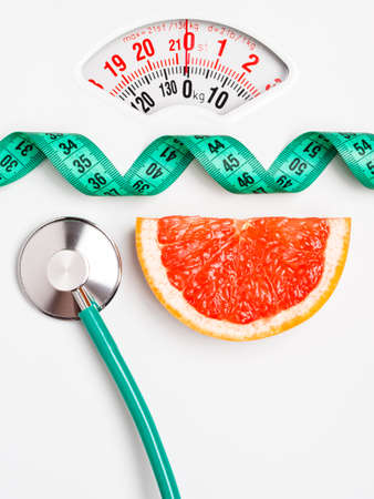 Diet healthy eating weight control concept. Grapefruit with measuring tape and stethoscope on white scalesの写真素材