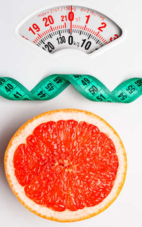 Dieting healthy eating slim down concept. Closeup grapefruit slice with measuring tape on white weight scaleの写真素材