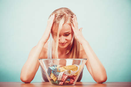 Diet, healthy eating, weight loss and slim body concept. Fit fitness girl and bowl with many colorful measuring tapes, young woman bored of dieting Diet, healthy eating, weight loss and slim body concept. Fit fitness girl and bowl with many colorful measuring tapes, young woman bored of dieting