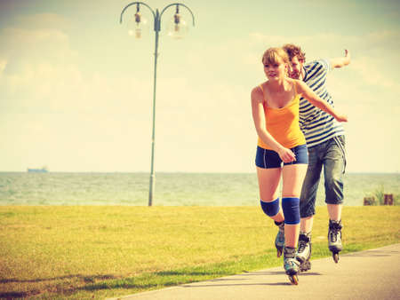 Holidays, active people and friendship concept. Young fit couple on roller skates riding outdoors on sea shore, woman and man rollerblading together on the promenadeの写真素材