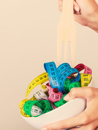 Diet, healthy eating, weight loss and slim body concept. Human hand holding bowl with many colorful measuring tapesの写真素材