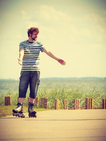 Holidays, active lifestyle freedom concept. Young fit man on roller skates riding outdoors on sea coast, guy rollerblading on sunny dayの写真素材