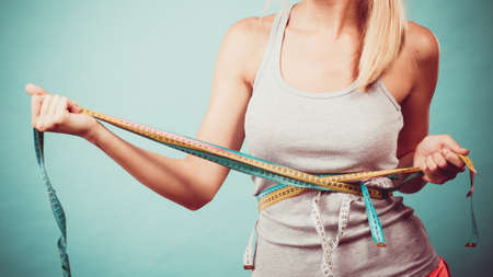 Weight loss, slim body, healthy lifestyle concept. Fit fitness girl measuring her waistline body with many colorful measure tapes on blueの写真素材