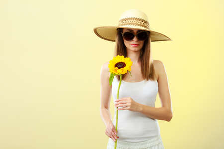Closeup of attractive summer woman in sunglasses straw hat with sunflower in her hand on yellow backgroundの写真素材