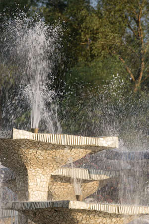 Closeup of stone fountain with dripping water and green trees backgroundの写真素材
