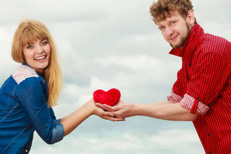 Love and happiness concept. Woman and man young hipster couple in love playing sharing free time having fun holding red heart, outdoor against skyの写真素材