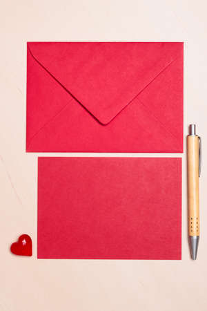 Red blank sheet of paper with envelope and little heart, pen on wooden surface. Background for valentines day or wedding card.の写真素材