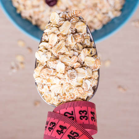 Diet healthy food weight loss concept. Oatmeal in blue bowl and pink measuring tape around spoon on kitchen table, top viewの写真素材