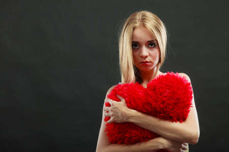 Broken heart love concept. Sad unhappy woman hugging red heart pillow dark backgroundの写真素材