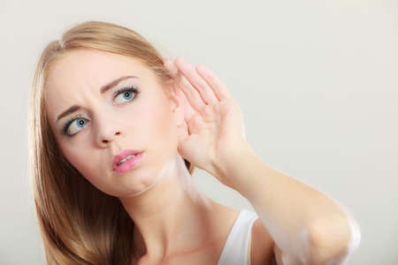 Closeup female hand to ear listening on gray. Gossip girl with palm behind ear spying. Young woman listening secret.の写真素材
