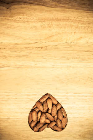 Whole food, good for health. Heart shaped almonds on wooden surface board backgroundの写真素材