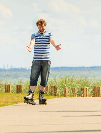 Holidays, active lifestyle freedom concept. Young fit man on roller skates riding outdoors on sea coast, guy rollerblading on sunny dayの写真素材