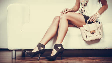 Elegant outfit. Female fashion. Girl in fashionable clothes sitting on sofa holding bag handbag.の写真素材