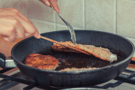 Human frying breaded chicken cutlet on fry pan. Person making dinner meal.の写真素材
