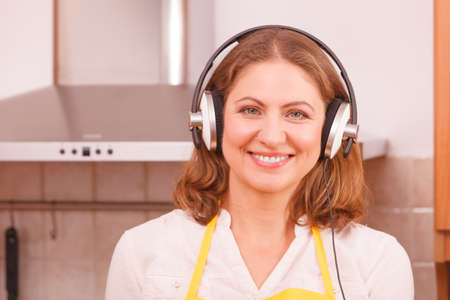 Cooking and preparing food concept. Happy relaxed beauty woman housewife chef with earphones listening music in house kitchen making dinner meal.の写真素材