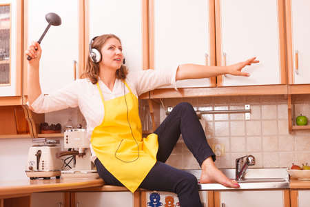 Relax in kitchen. Listening music singing and dancing. Funny happy housewife cook chef with earphones wearing yellow apron sitting and relaxing at home.の写真素材