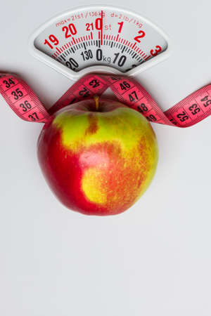 Dieting healthy eating slim down concept. Closeup apple with measuring tape on white weight scaleの写真素材