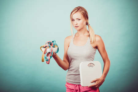 Diet, healthy eating and slim body concept. Fit fitness girl holding bowl with many colorful measuring tapes as dieting symbol and weight scales studio shot on blueの写真素材