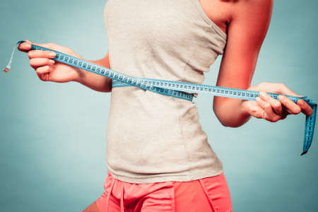 Weight loss, slim body, healthy lifestyle concept. Fit fitness girl measuring her waistline with measure tape on blueの写真素材