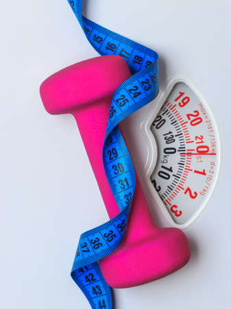 healthy lifestyle fitness weight control concept. Closeup pink dumbbell with blue measuring tape on white scalesの写真素材