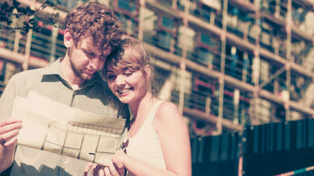 Real estate and family concept - young couple on front of new big modern house with blueprint project dreaming about homeの写真素材