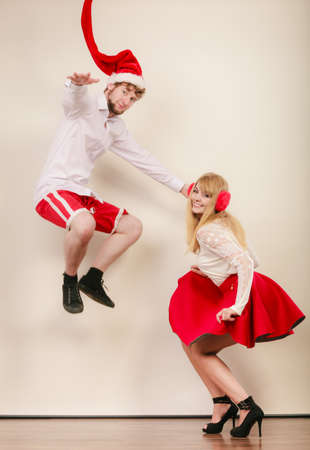 Happy cute couple dancing and jumping in studio. Pretty woman and handsome man in santa claus hat having fun. Christmas xmas season.の写真素材