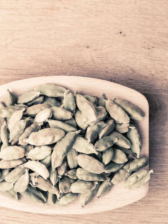 Green cardamom pods heap on wooden spoon rustic table backgroundの写真素材