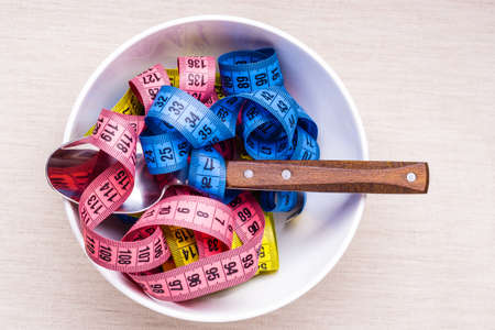 Diet food healthy lifestyle and slim body concept. Many colorful measuring tapes in bowl on table with fork, top viewの写真素材