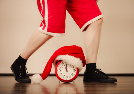 Closeup of man legs and alarm clock with santa claus hat. Christmas time season concept.  