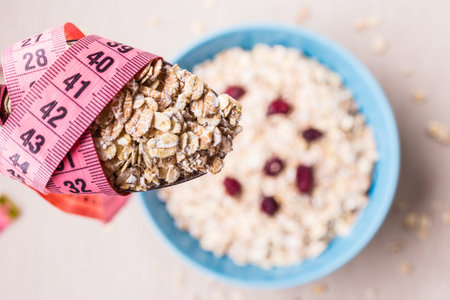 Diet healthy food weight loss concept. Oatmeal in blue bowl and pink measuring tape around spoon on...