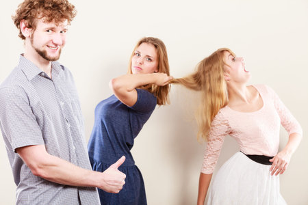 Aggressive mad women fighting over man pulling hair. Young jealous girls wooing guy. Violence.の写真素材