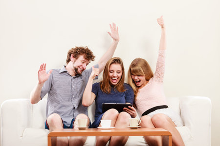 Successful happy friends with hands up browsing surfing internet on tablet. Young people man guy and...