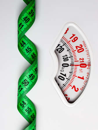 Dieting weightloss slim down concept. Closeup measuring tape on white weight scaleの写真素材