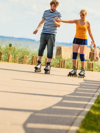 Holidays, active people and friendship concept. Young fit couple on roller skates riding outdoors on...