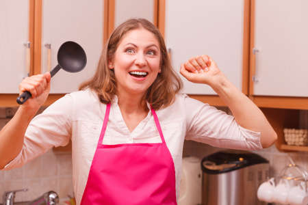 Cooking and preparing food meal concept. Happy successful smiling woman chef cook housewife holding ladle spoon with hands fists up gesture in kitchen.の写真素材