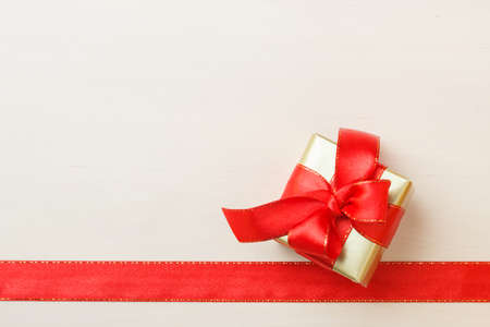 Holidays, present concept. Small golden box with gift tied decorative bow and red ribbon frameの写真素材