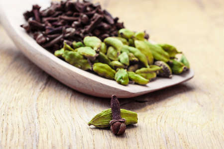 Green cardamom pods and cloves on wooden spoon rustic table backgroundの写真素材