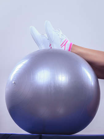 Sport, training, gym and lifestyle concept. Female legs in sneakers on fitball, woman in sportswear doing fitness exercises with fit ball at homeの写真素材
