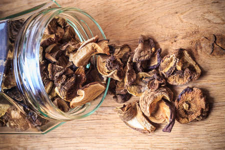 Food. Closeup dry mushrooms spilling out from storage jar on wooden surface table background.の写真素材