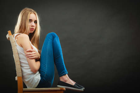 Loneliness negative emotion concept. Young sad lonely woman sitting huddled on chairの写真素材