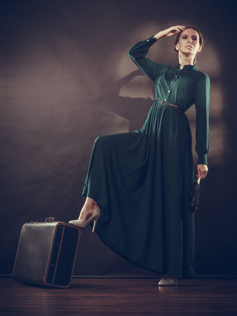 Woman retro style long dark green gown with old suitcase and feather fan, vintage photoの写真素材