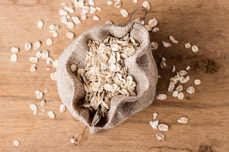 Dieting. Oat cereal in burlap sack on wooden surface, top, view. Healthy food for lowering...