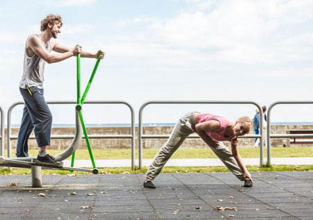 Active young man exercising on elliptical trainer machine and woman stretching. Muscular sporty guy...