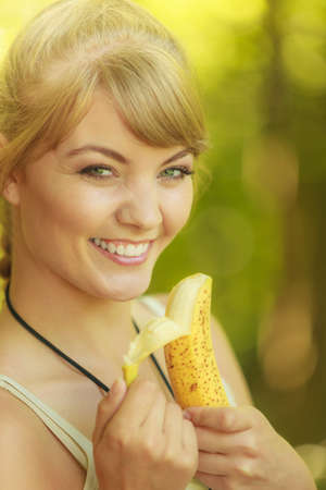 Adventure, tourism, enjoying summer time - young tourist hiker woman eating banana fruit in forest trailの写真素材